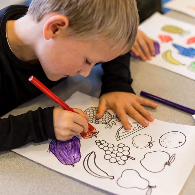 Barn farvelægger tegninger af frugt og grønt