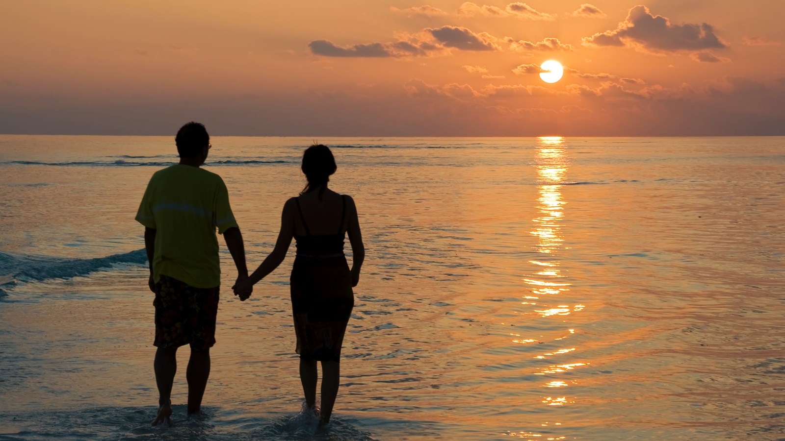 Par holder i hånd ved solnedgang i vandkanten