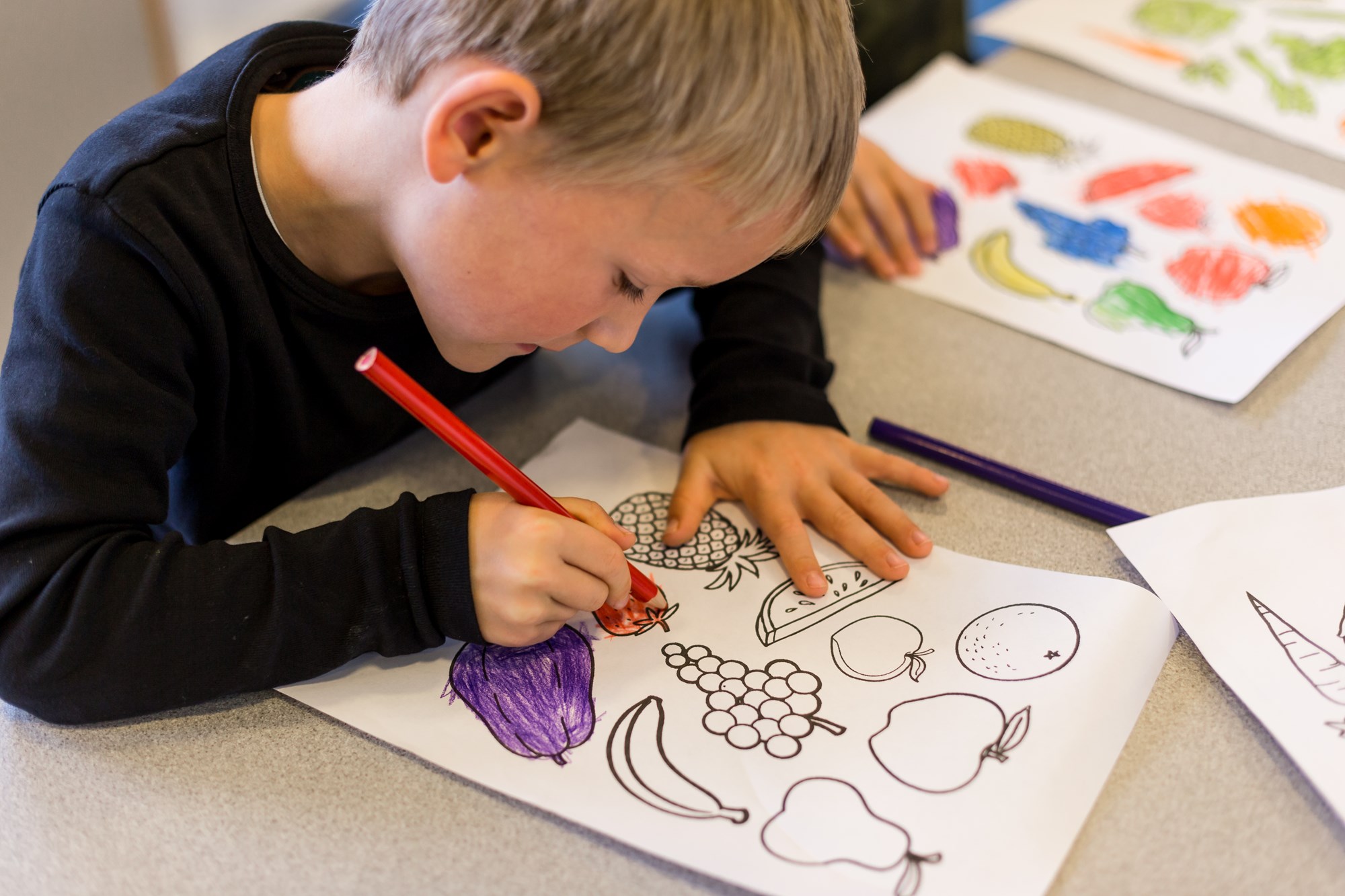 Barn farvelægger tegninger af frugt og grønt