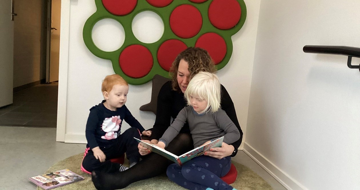 To børn læser i bog sammen med personale