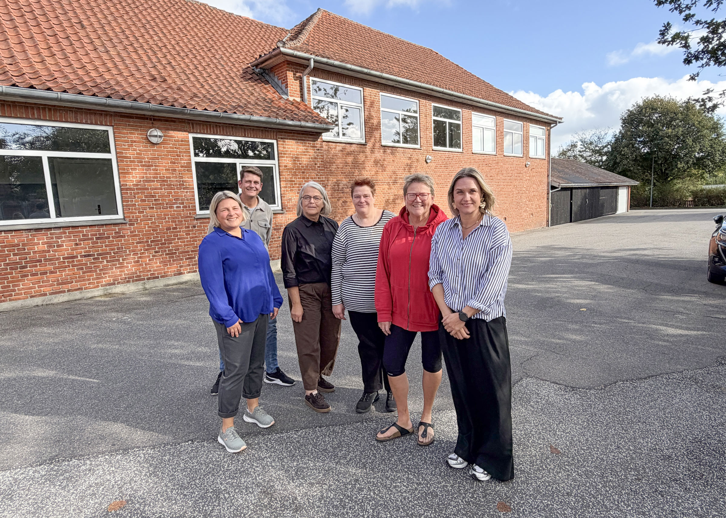 Billedtekst: Fra venstre: Tanja Kjær Larsen fra Frivillighuset, Jonas Nesager Røge og Tenna Vad fra Familiecentret, Maibritt Christensen og Hanne Jensen fra Halvrimmen Landsbyråd og Ann Bonnerup fra Familiecentret. I baggrunden Familienetværkets mødested: Gymnastiksalen ved den gamle skole i Halvrimmen – nu tilholdssted for blandt andre Familiecentret. ...