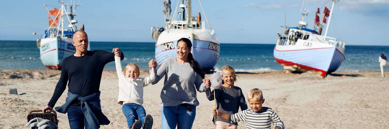 Familie med tre børn på strand med fiskerbåde