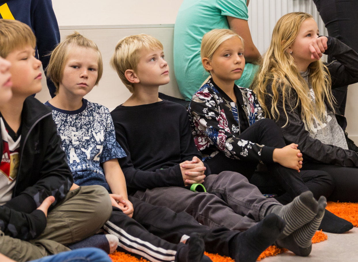 Børn sidder på gulvet og lytter