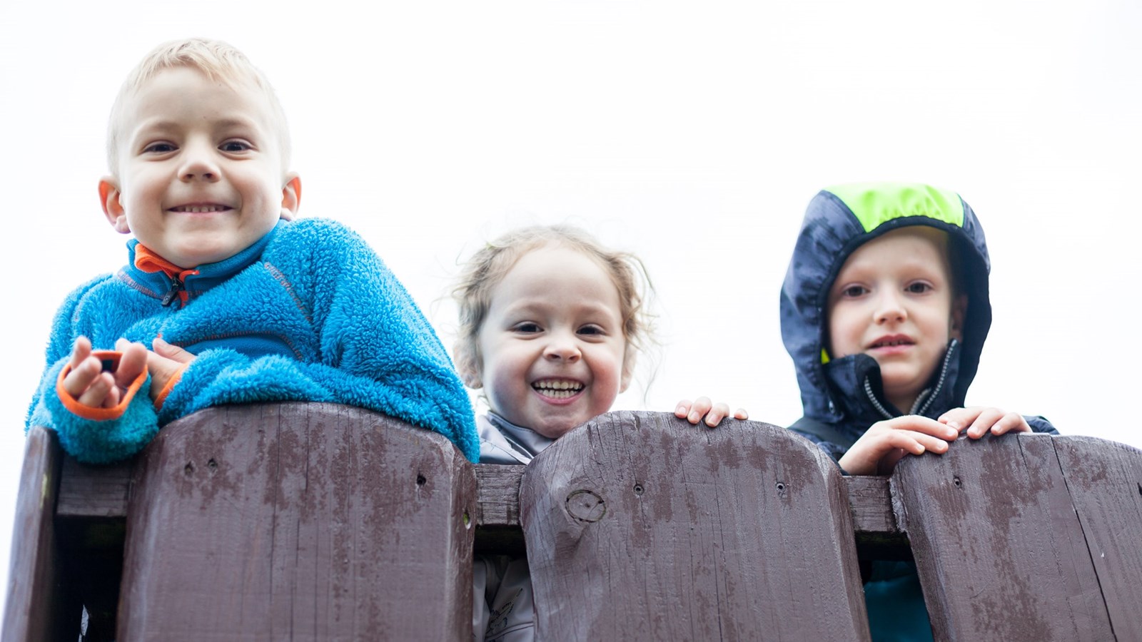 tre børn læner sig op af hegn