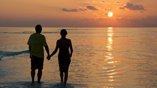Par holder i hånd ved solnedgang i vandkanten