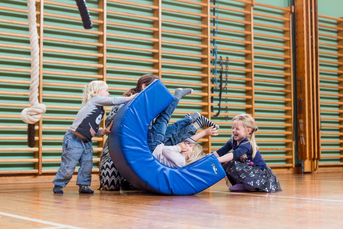 Børn og forælder leger på redskab i gymnastiksal